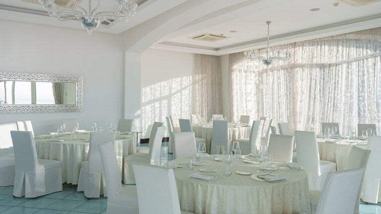 Il Golfo's white dining room with round tables and large windows, Hotel Raito