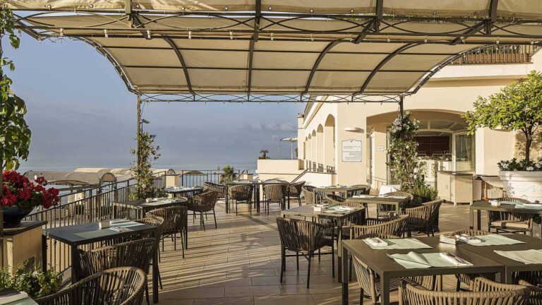 A covered restaurant terrace with tables and a view down the coast, Hotel Raito