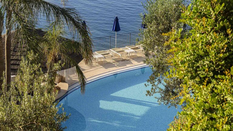 The outdoor pool seen from above through palms, with the sea beyond, Hotel Raito