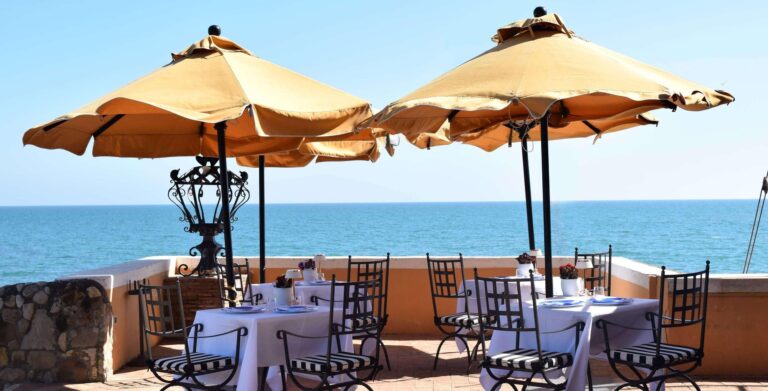 Tables under parasols on the restaurant terrace facing the sea, La Posta Vecchia Hotel