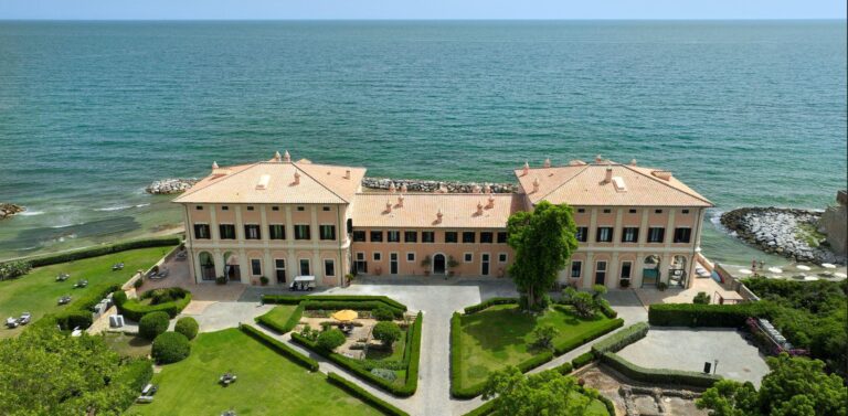 The seafront facade and lawns seen from above the water at Palo Laziale, La Posta Vecchia Hotel