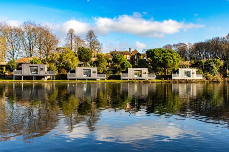 The Lakeside Lodges on the bank of the Great Water, reflected in the lake on a clear winter day, Leeds Castle