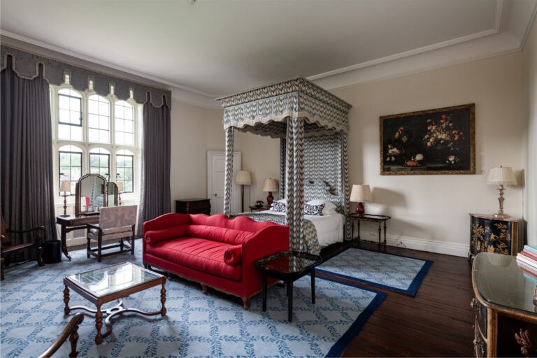 A Castle State bedroom with a patterned four-poster, a red sofa and a flower still life on the wall, Leeds Castle