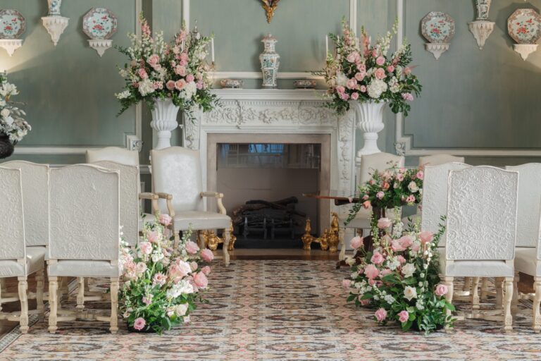 Pink and white flowers either side of the aisle in the Ceremony Room, with the fireplace and registrar's table behind, Leeds Castle