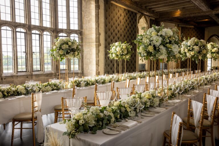 Long tables with tall white flower arrangements in the Salon, beside its leaded windows over the moat, Leeds Castle