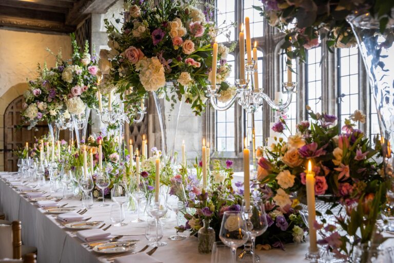 A long candlelit table in the Castle, with tall mixed flowers and glass candelabra beneath leaded windows, Leeds Castle