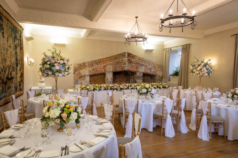 A Maiden's Tower wedding room set with round tables, a top table under the brick Tudor fireplace and a tapestry on the wall, Leeds Castle