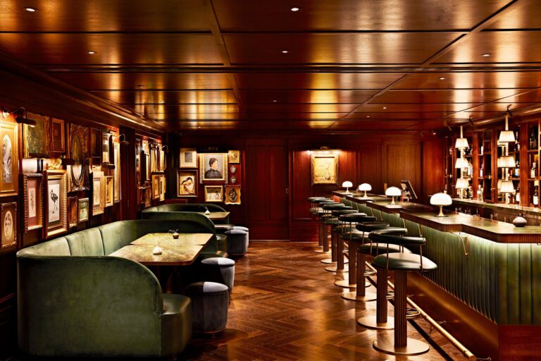 A wood-panelled bar with green leather banquettes, bar stools and framed art on the walls, Mandarin Oriental Hyde Park