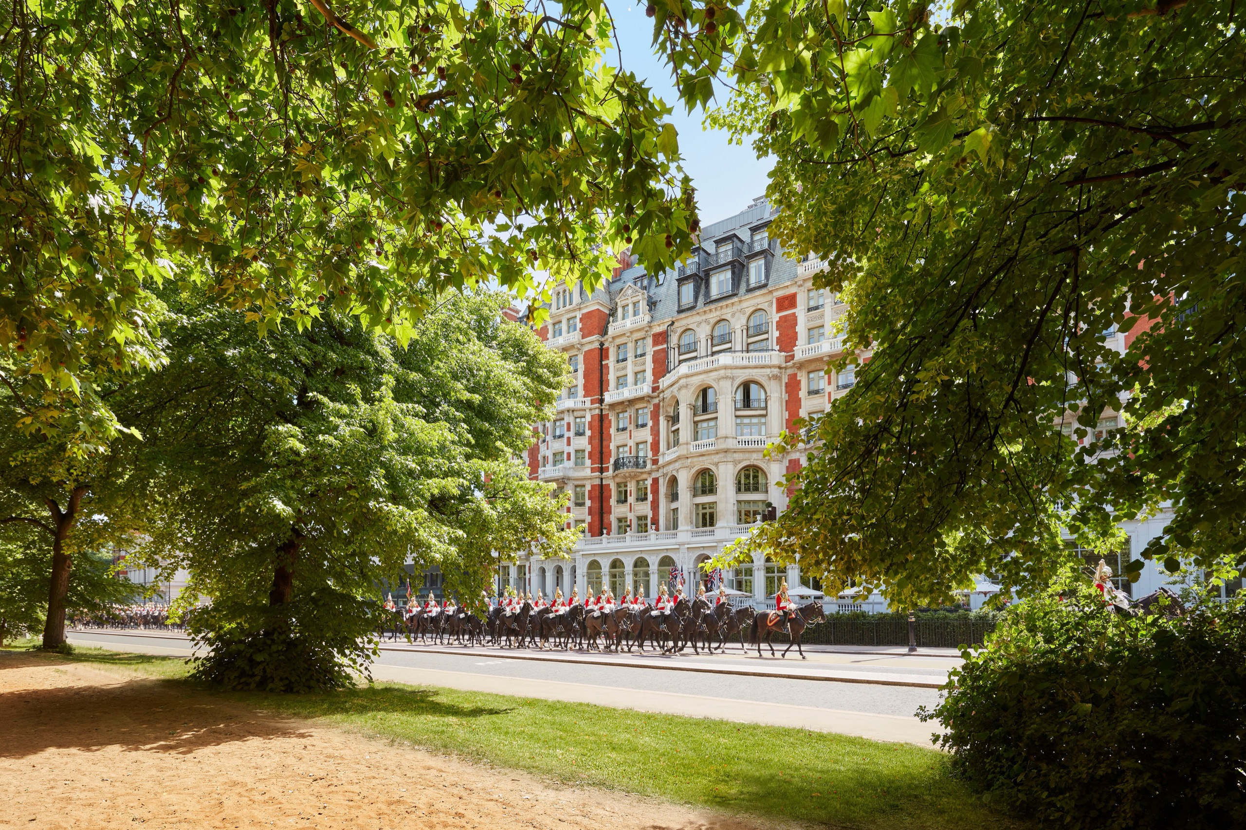 The park-side facade seen through the trees of Hyde Park, with mounted riders passing on the carriageway, Mandarin Oriental Hyde Park