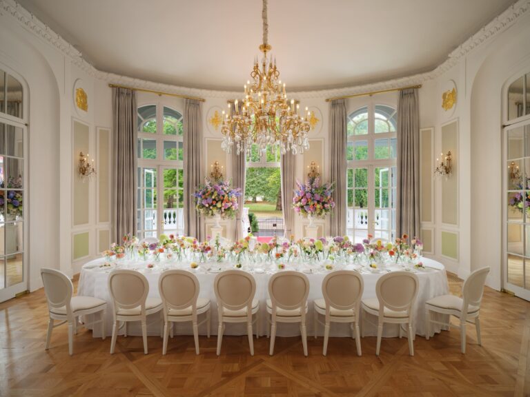 A single long dining table dressed with flowers beneath a chandelier in the Loggia, Mandarin Oriental Hyde Park
