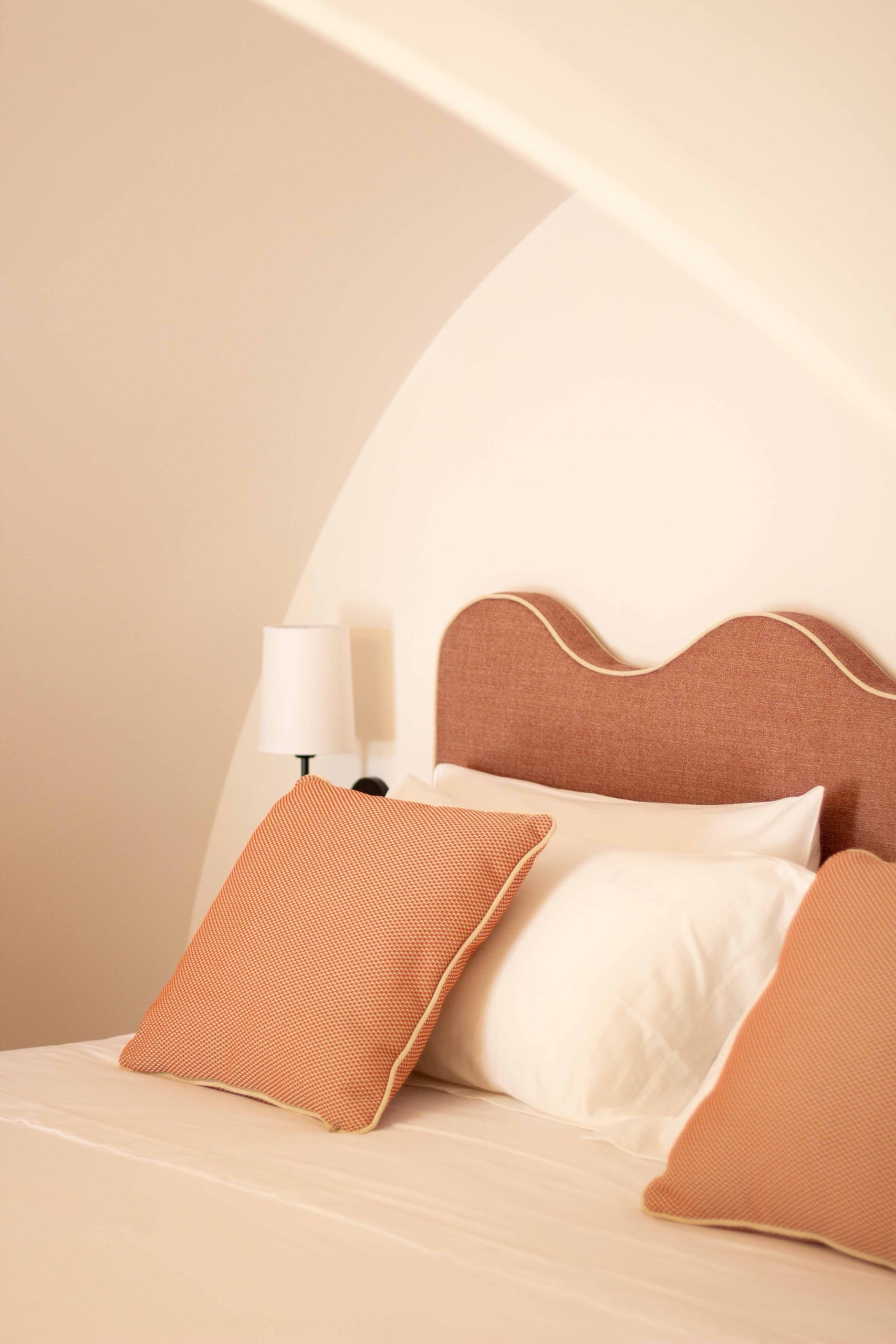 A scalloped terracotta headboard with terracotta cushions and a wall lamp, Masseria Don Luigi