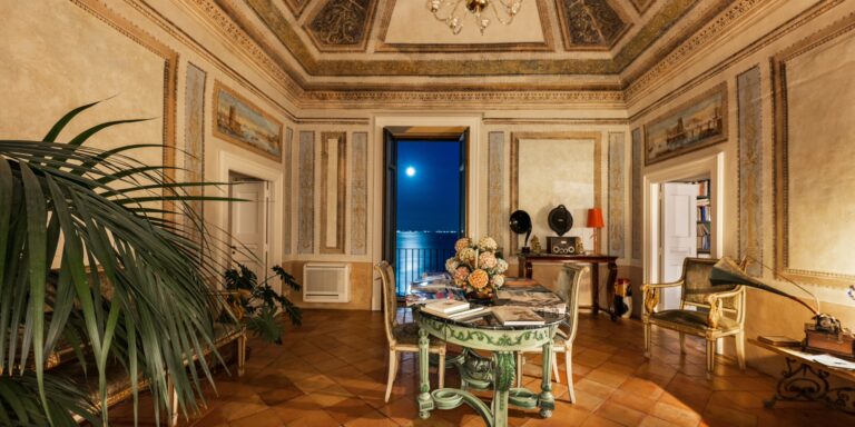 Frescoed salon with painted panels, terracotta floor and an open door to the sea at night, Palazzo Suriano