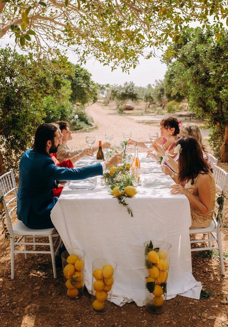 Guests at a white-clothed table decorated with lemons under the olive trees, Pittalumari Makari