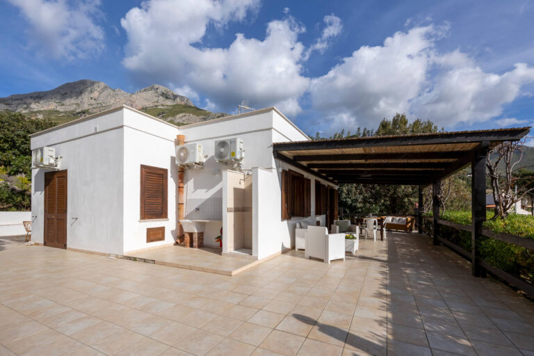 Casa del Mandorlo, a white single-storey cottage with a cane-roofed veranda, below the mountains, Pittalumari Makari