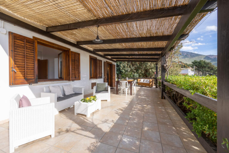 The long covered veranda of Casa del Mandorlo with sofas and a table facing the garden, Pittalumari Makari