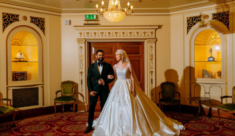 A bride and groom posing in a panelled room with arched niches and a small chandelier, Plaisterers' Hall