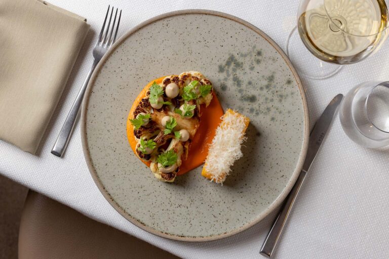 A small plated starter on a grey plate beside a glass of white wine, Plaisterers' Hall