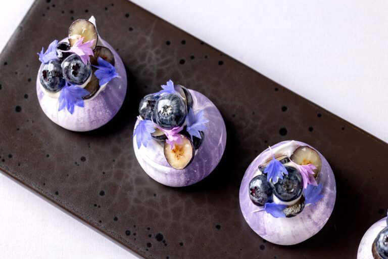 Three small desserts topped with blueberries and edible flowers on a dark board, Plaisterers' Hall