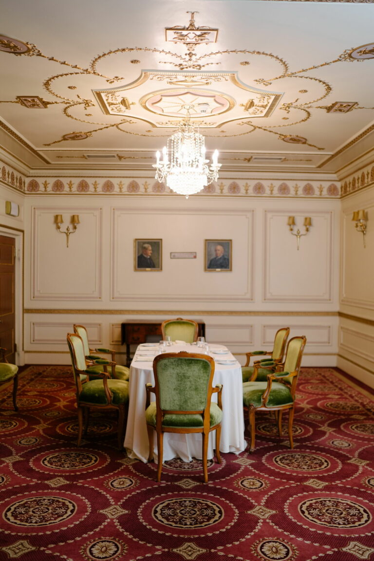 The Mott Room with a round table and green chairs beneath a plasterwork ceiling, Plaisterers' Hall