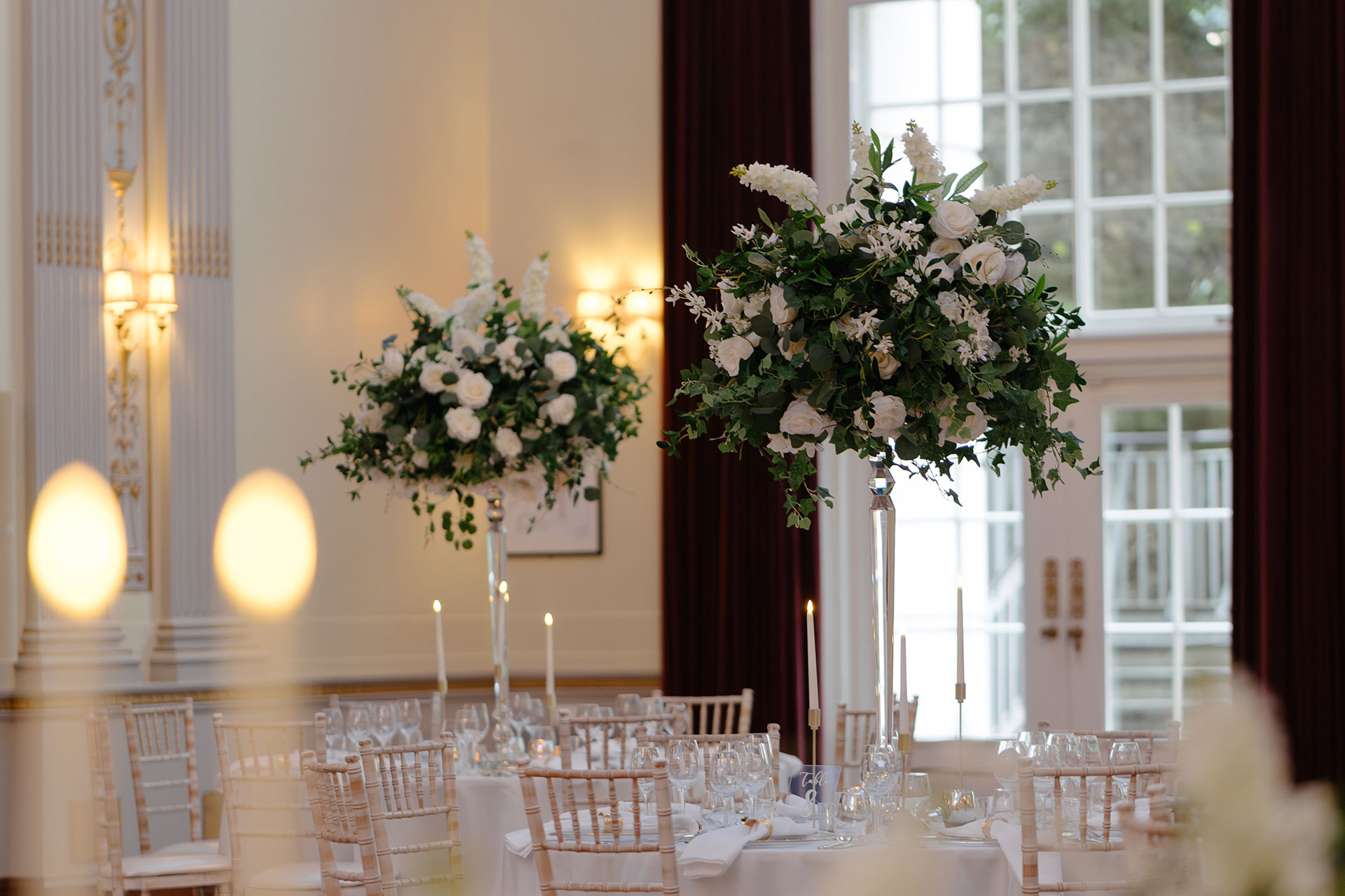 Round tables with tall white floral arrangements beside the long windows of the Great Hall, Plaisterers' Hall