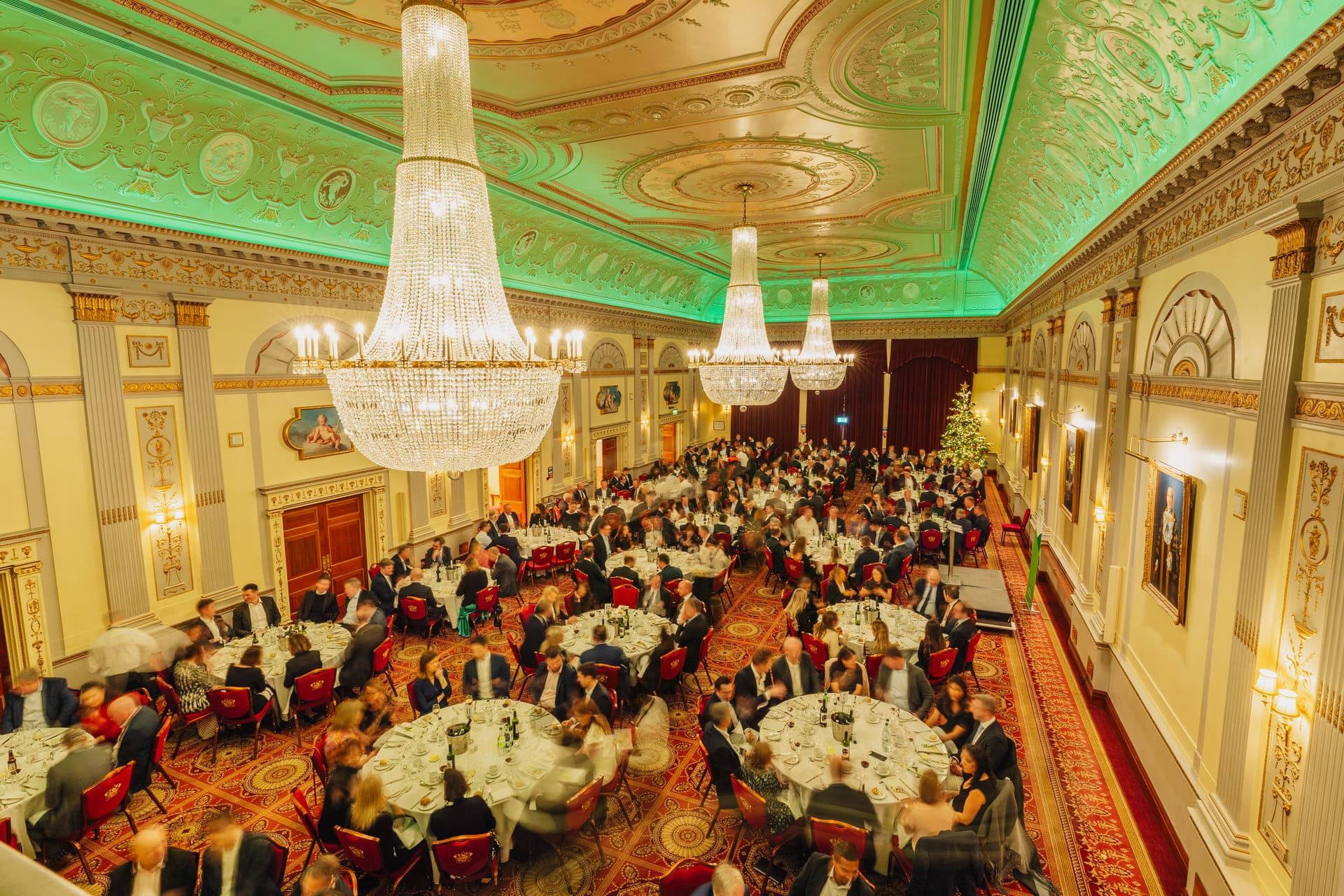 A full seated dinner in the Great Hall seen from the gallery, with green uplighting on the ceiling, Plaisterers' Hall