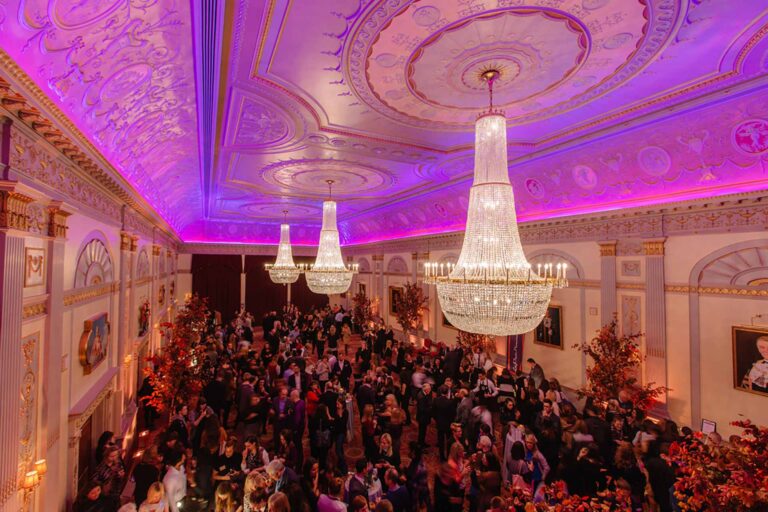 A crowded party in the Great Hall under purple lighting and chandeliers, Plaisterers' Hall