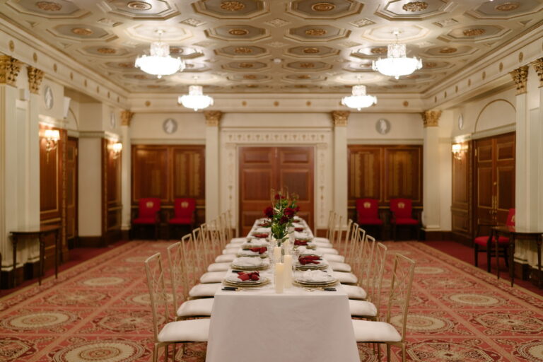 A long dinner table with clear chairs down the centre of the Livery Hall, under a coffered ceiling, Plaisterers' Hall