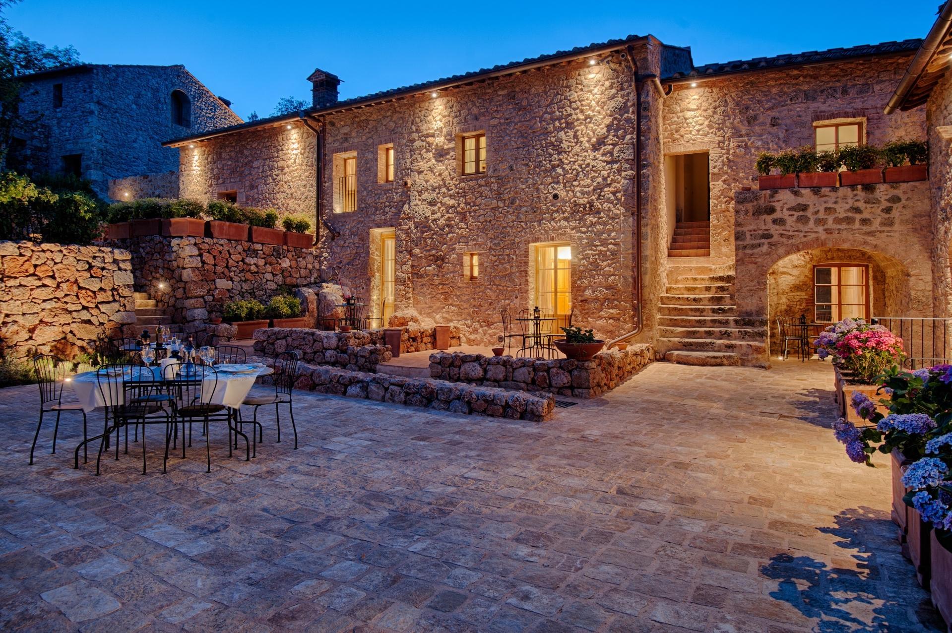 Stone courtyard at dusk with a laid table, stone steps and potted hydrangeas, Relais La Costa