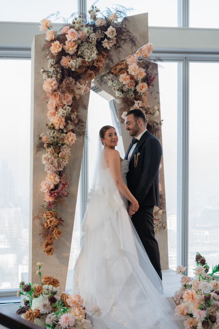 A wedding couple under a floral arch of pale roses against the windows, Shangri-La The Shard, London