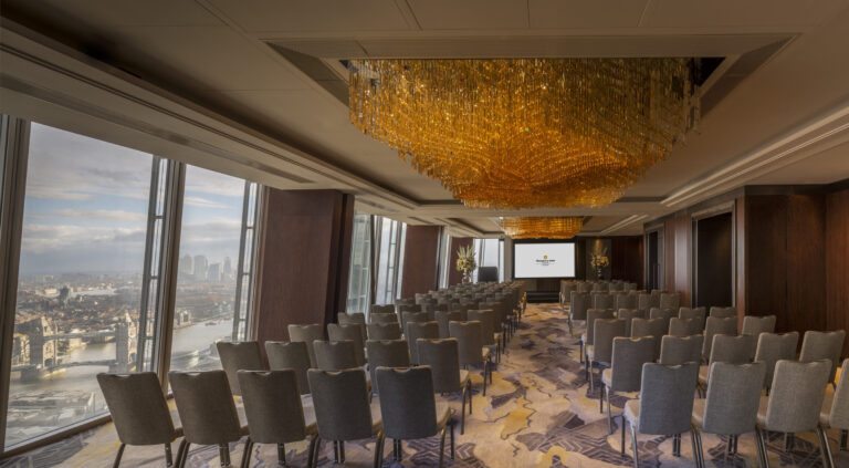 A long event space with gold chandeliers laid out in rows of chairs, with Tower Bridge through the windows, Shangri-La The Shard, London