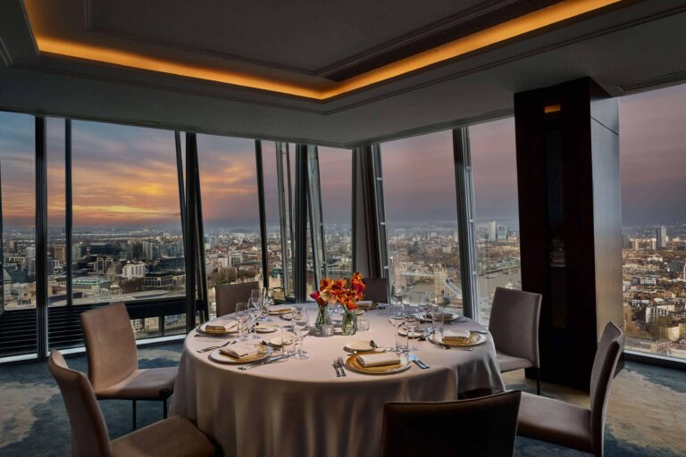 A round table laid for a small dinner at sunset, with Tower Bridge and the river through the windows, Shangri-La The Shard, London