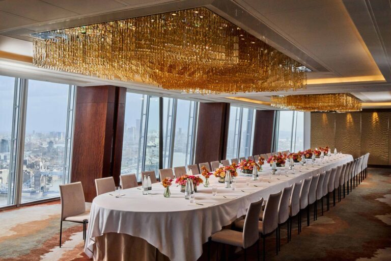 A single long banquet table under a gold chandelier, set with orange flowers beside the windows, Shangri-La The Shard, London