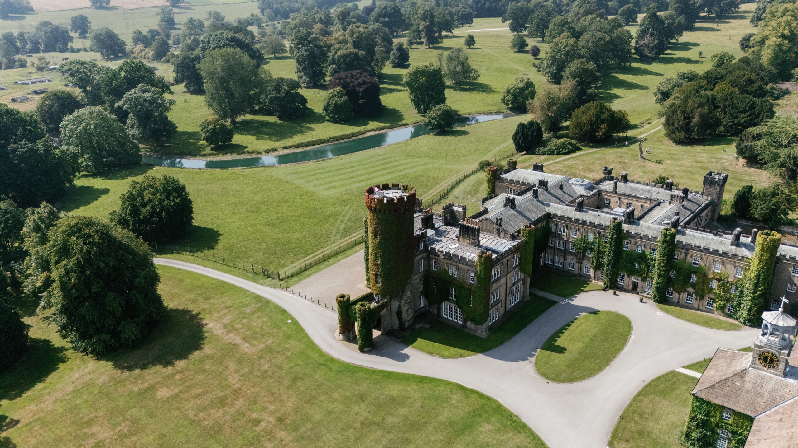 Aerial view of the castle, its round tower and the drive, with the serpentine lake and parkland behind, Swinton Park
