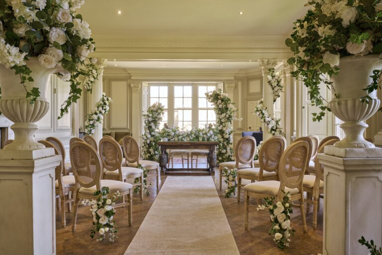 The Panelled Room set for a civil ceremony, with stone urns of white flowers either side of the aisle, Swinton Park