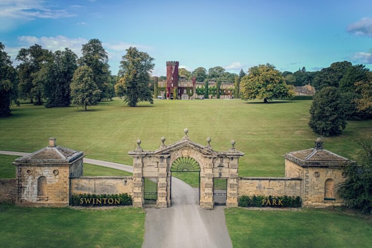 The stone gateway and lodges at the park entrance, with the castle beyond open parkland, Swinton Park