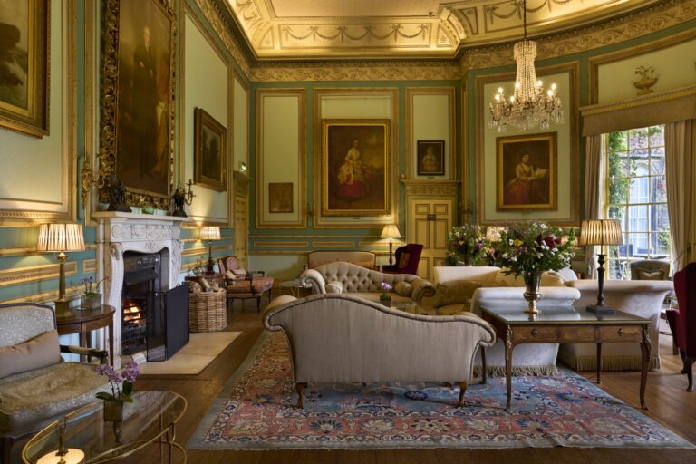 The Drawing Room, with gilded cornices, a chandelier, family portraits and an open fireplace, Swinton Park