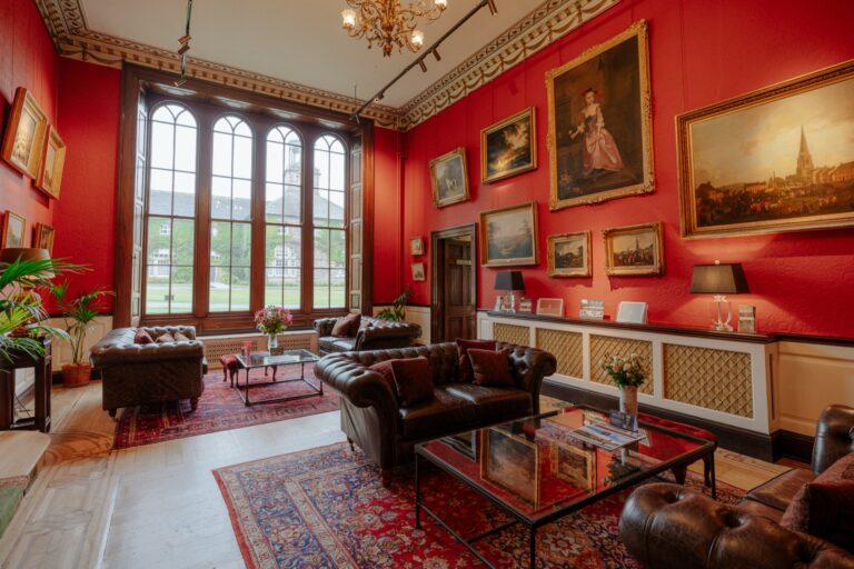 The red-walled Lower Hall with leather sofas, oil paintings and tall arched windows, Swinton Park