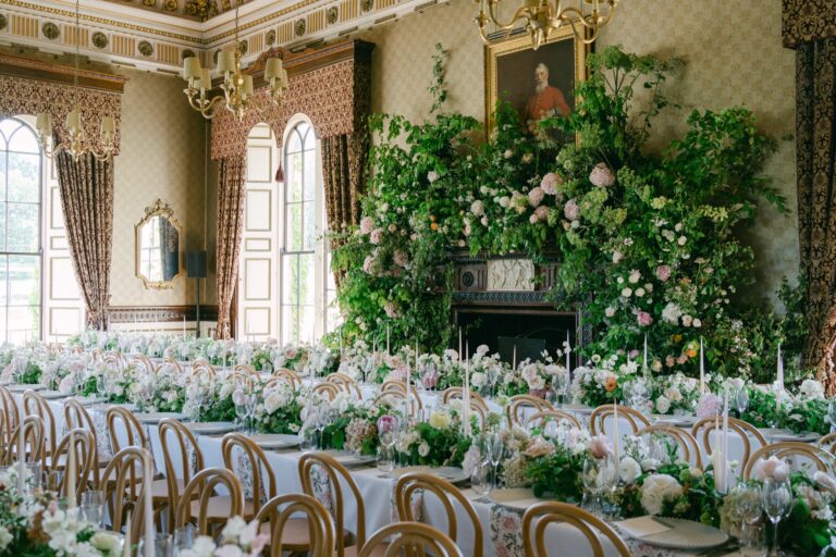 Long tables in Samuel's Restaurant dressed with flowers for a wedding breakfast, with greenery around the fireplace, Swinton Park