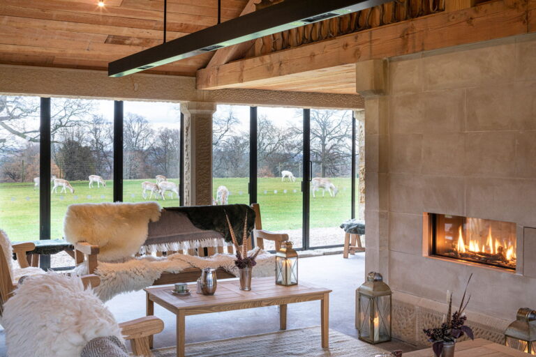 The Deer House lounge with its fireplace, sheepskins and glass walls, with deer grazing outside, Swinton Park