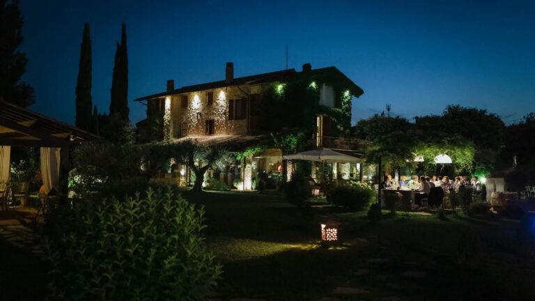The farmhouse lit at night with guests dining in the garden, Tenuta San Masseo