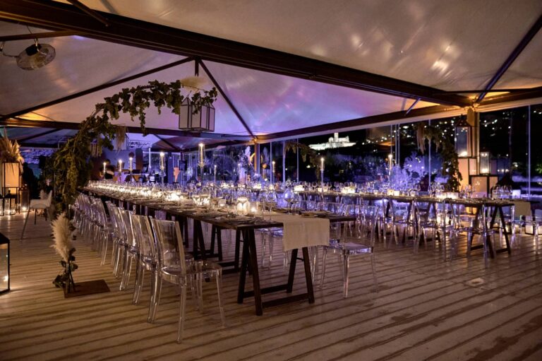 Long dinner tables with clear chairs inside the Vista Cube, lit at dusk, Tenuta San Masseo