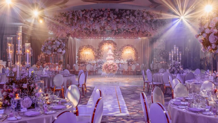 The Ballroom lit in violet with a floral stage, a raised aisle and candlelit tables, The Dorchester