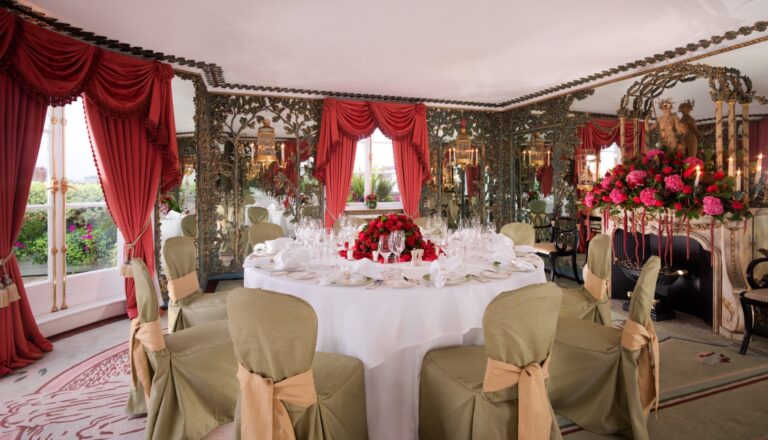 A round table laid for dinner in The Penthouse between red drapes and mirrored panels, The Dorchester