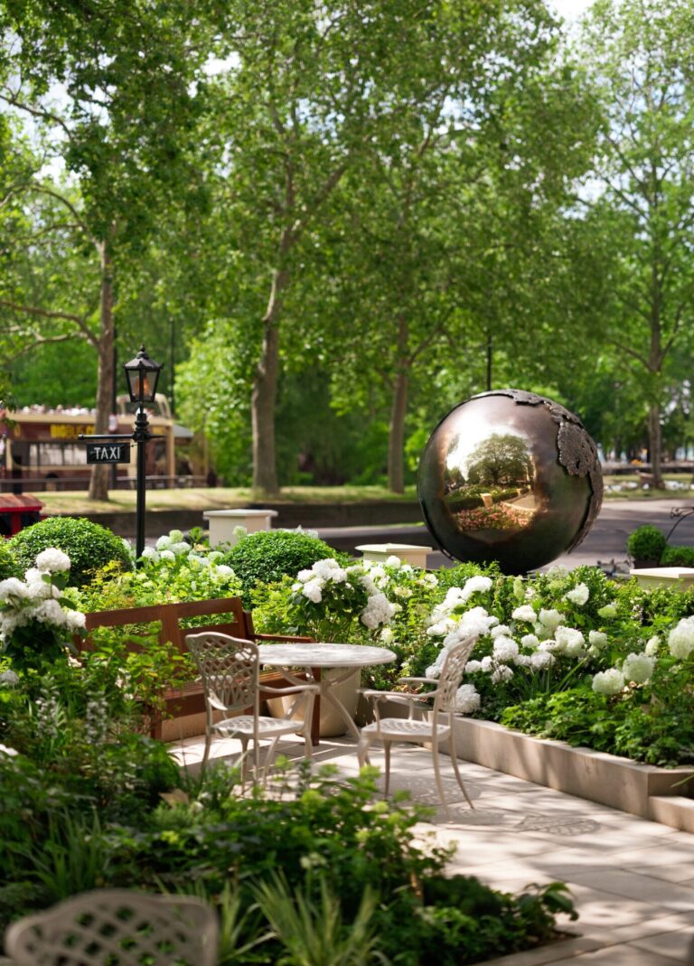 The hotel gardens with a mirrored sphere sculpture among trees and white flowers, The Dorchester