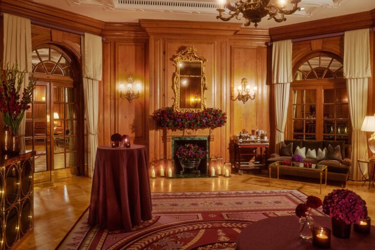 The oak-panelled Holford Room set for drinks, with red flowers and candles by the fireplace, The Dorchester