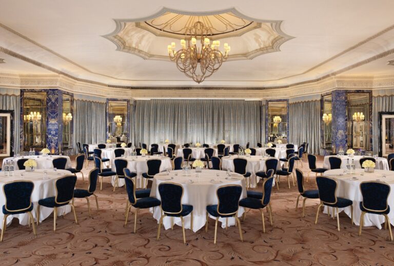 Round tables with dark blue chairs set out across the Ballroom under its domed ceiling, The Dorchester