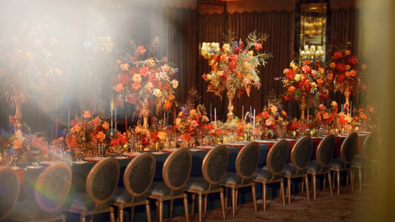 A long dinner table heaped with orange and pink flowers under warm lighting, The Dorchester