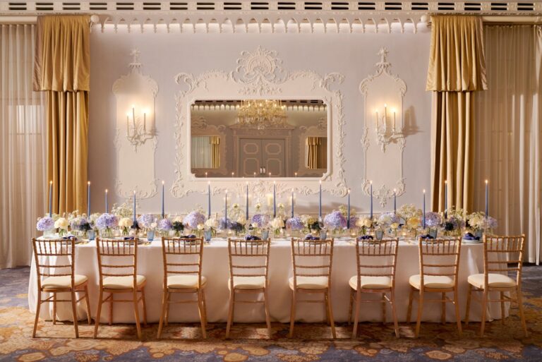 A long table with candles and flowers set against the carved white wall of the Orchid Room, The Dorchester