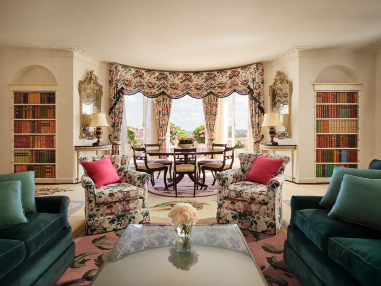 The living room of The Oliver Messel Terrace Suite with a bay window, bookshelves and green sofas, The Dorchester