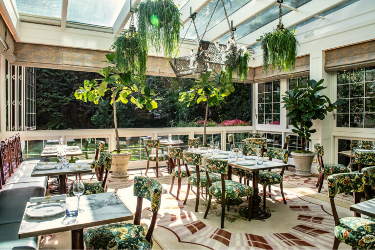 The Veranda under its glass roof, with small tables, potted trees and windows onto the garden, The Goring